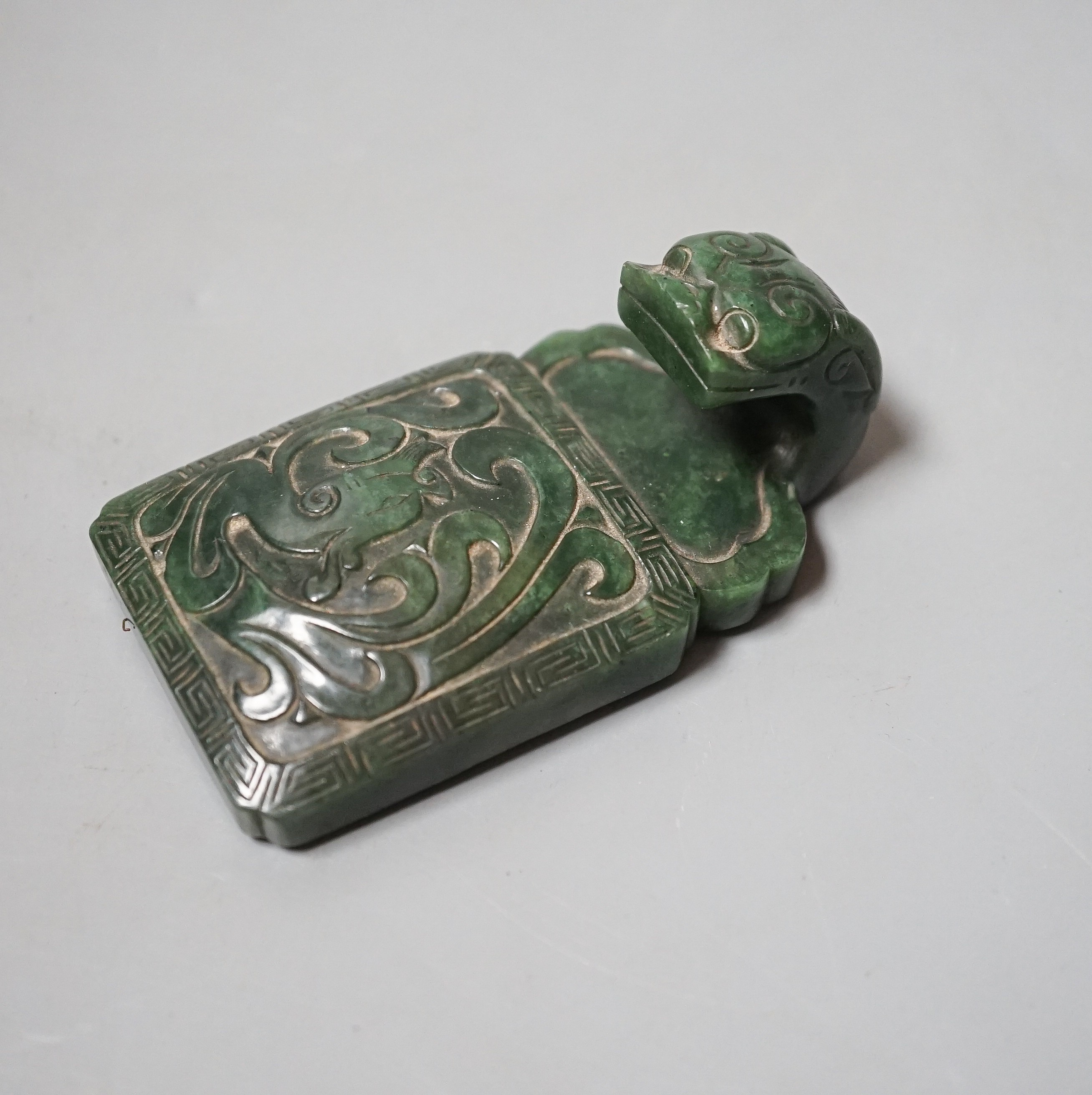 A Chinese spinach green jade belt hook, 19th century, in archaistic style, carved in relief with a chi-dragon, with a dragon head handle, 9cm